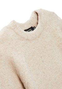 Pull en maille beige fabriqué à partir d'un matériau doux, avec un col rond côtelé et une surface texturée parsemée de petites touches de couleur claire.