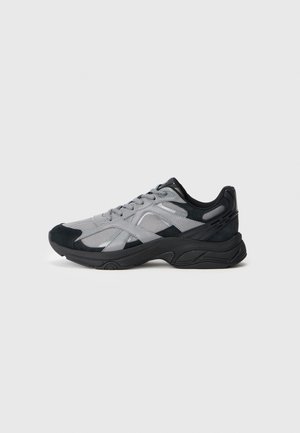 Zapatillas deportivas para hombre en gris y negro, con paneles de malla y ante, suela gruesa y cierre de cordones, exhibidas sobre un fondo blanco.