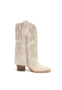 Botas de tobillo de ante sintético beige con diseño decorativo de tachuelas, punta afilada, tacón ancho de altura media y cierre con cremallera lateral.