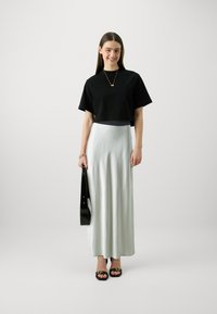 Svart croppet t-skjorte, lys grønn satin maxiskjørt, svarte sandaler og en svart håndveske. Glatt stoff med en avslappet passform og flytende design.