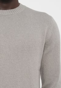 Hellgrauer gestrickter Pullover mit Rundhalsausschnitt, der über eine gerippte Textur und lange Ärmel verfügt. Keine sichtbaren Muster oder Akzente.