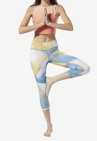 Lekki, dopasowany sportowy top w kolorze bladego różu, połączony z legginsami kapri w wielokolorowe geometryczne wzory w odcieniach niebieskiego, żółtego i białego.