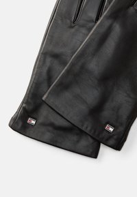 Guanti in pelle nera con una texture liscia, forma allungata, con un piccolo logo sulla cuffia e tre aperture per le dita.
