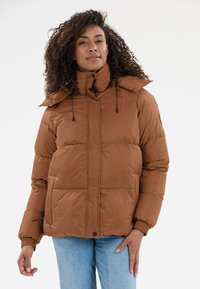 Brun pufferjakke med højt krave, vandret syninger, justerbare snore og elastiske manchetter. Båret over blå jeans.