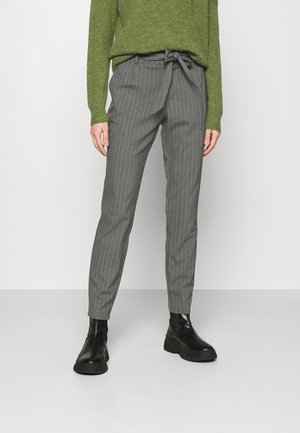 Gråstribede bukser med bindebånd i taljen, kombineret med en grøn trøje. Skoene er sorte med en glat tekstur og kraftige såler.