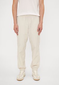 Beiga byxor med elastisk midja, samlade manschetter och sidofickor, gjorda av lättviktig tyg. Matchas med ljusa sneakers.