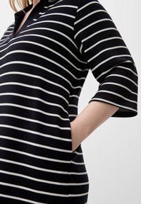 Abito a righe bianche e nere con scollo a V, maniche a tre quarti e tasche laterali; tessuto strutturato con righe orizzontali.