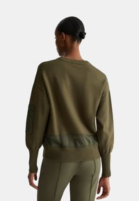 Maglione over-size verde oliva con collo e polsini a coste. Presenta un corpo texture e accenti in tessuto liscio all'orlo e alle maniche.