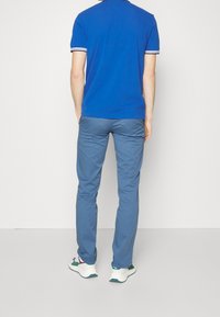 Blå pikétröja med vit och marinblå randig krage, ihopparad med ljusblå byxor. Skor är vita sneakers med gröna och lila accenter.