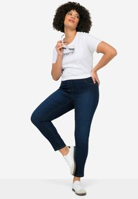 Jeggings azul oscuro de denim con un corte ajustado, que presentan detalles de costura, combinados con una camiseta blanca de manga corta.