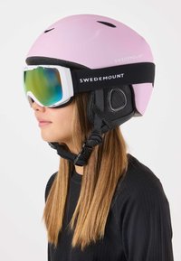 Pink ski helmet with vent holes, black chin strap, and a black accent. Features large ski goggles with a reflective, tinted lens.