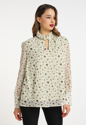 Blomstret bluse i lysegrøn, med en halsbånd og nøglehulsgodkendelse. Lange ærmer, gennemsigtig stof og spredte rosa og grønne blomsterprint.