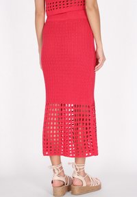 Gebreide, hoog taille-midirok in felroze met open structuur, patroontextuur en een rechte pasvorm, gecombineerd met lichtgekleurde espadrille-sandalen.