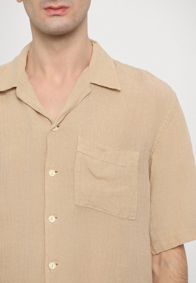 Short-sleeve, beige linen shirt with a relaxed collar, front pocket, and five buttons. Fabric has a soft, textured appearance.