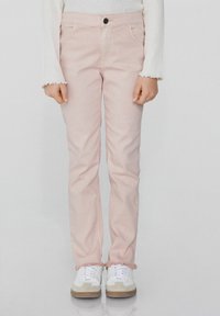 Světle růžové džíny s rovným střihem, roztrhanými lemy a předními kapsami, zkombinované s bílými teniskami s béžovým akcentem.