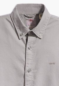Camisa de botón gris claro hecha de una mezcla de algodón. Presenta un cuello con solapas, dos cierres de botón y un pequeño logo de Levi's bordado.