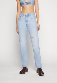 Ljusblå högmidjade jeans med ett slitet knä, kombinerat med mörkbruna träskor med silvernitar. Slät denimstruktur.