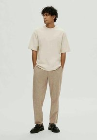 Gaiši brūns īsām piedurknēm krekls ar apaļu izgriezumu, apvienots ar gaiši brūnām raibām biksēm un melniem kurpēm ar sašūtām auklām. Gluda tekstūra.