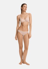 Reggiseno beige chiaro con stecche e spalline regolabili, abbinato a mutandine hipster coordinate. Texture liscia e design minimalista.