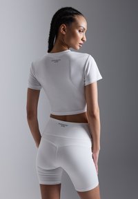 Hvit treningsantrekk bestående av en kortermet topp med cropped design og høyt liv shorts. Glatt tekstur med subtil merkevare på baksiden.