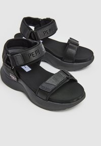 Sandalias deportivas negras con tiras ajustables, hechas de textil y goma, que cuentan con una suela acolchada y acentos del logo de la marca.