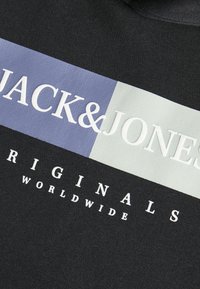 Tejido negro con un gran gráfico horizontal. Presenta "JACK&JONES" en blanco, con acentos en azul claro y verde claro, y "ORIGINALS WORLDWIDE" debajo.