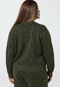 Olivgrüner Pullover mit einem Leopardenmuster in Schwarz. Aus gestricktem Stoff mit gerippten Bündchen und Saum gefertigt.
