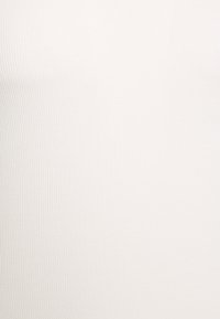 Vit ribbad linne i stretchigt material, med en åtsittande design och en subtil textur. Inga synliga logotyper eller mönster.