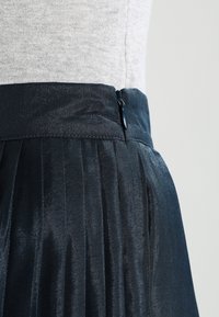 Černá plisovaná sukně s texturovaným leskem, vybavená pasem a bo�čním zipem pro zapínání. Tkanina se zdá být lehká a splývavá.