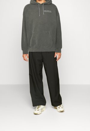 Koolgrijze hoodie met kangoeroezak en trekkoord, gecombineerd met zwarte wijde broek en lichtgekleurde sneakers.