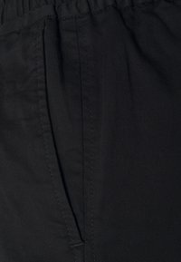 Close-up of black pants pocket with visible stitching and elastic waistband fabric.