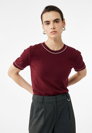 Haut en tricot bordeaux à manches courtes avec un col rond, présentant des coutures blanches contrastantes le long du col et des manches.