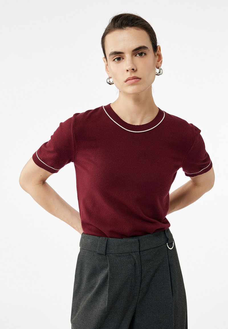 Top de punto burdeos de mangas cortas con cuello redondo, que presenta costuras blancas en contraste a lo largo del cuello y las mangas.