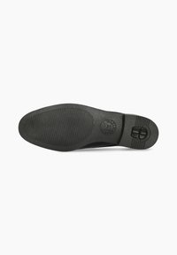Semelle de chaussure en caoutchouc noir à surface texturée, comportant un logo circulaire et un détail de boucle sur le côté, conçue pour l'adhérence et la durabilité.