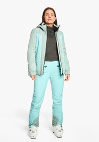 Hellblaues Skijacke mit Kapuze, kontrastierender dunkelgrauer Innenlage, passenden hellblauen Hosen und weißen Skischuhen mit sichtbarem Zubehör.