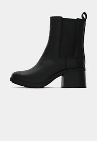 Stivale alla caviglia in pelle nera con tacco a blocco, pannello laterale elastico e linguetta sul retro su sfondo bianco.