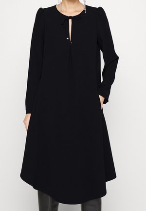 Černé šaty s dlouhými rukávy, s výstřihem ve tvaru klíčku a mašlí na límci. Hladká látka a áčkový střih.
