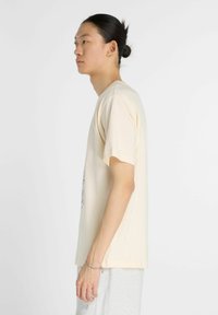 Kortærmet beige t-shirt lavet af bomuld, med et trykt design foran, afslappet pasform og rund halsudskæring.