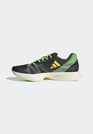 Chaussure de course noire et verte avec des accents jaune néon, des lacets verts et une semelle blanche rembourrée sur un fond clair uni.
