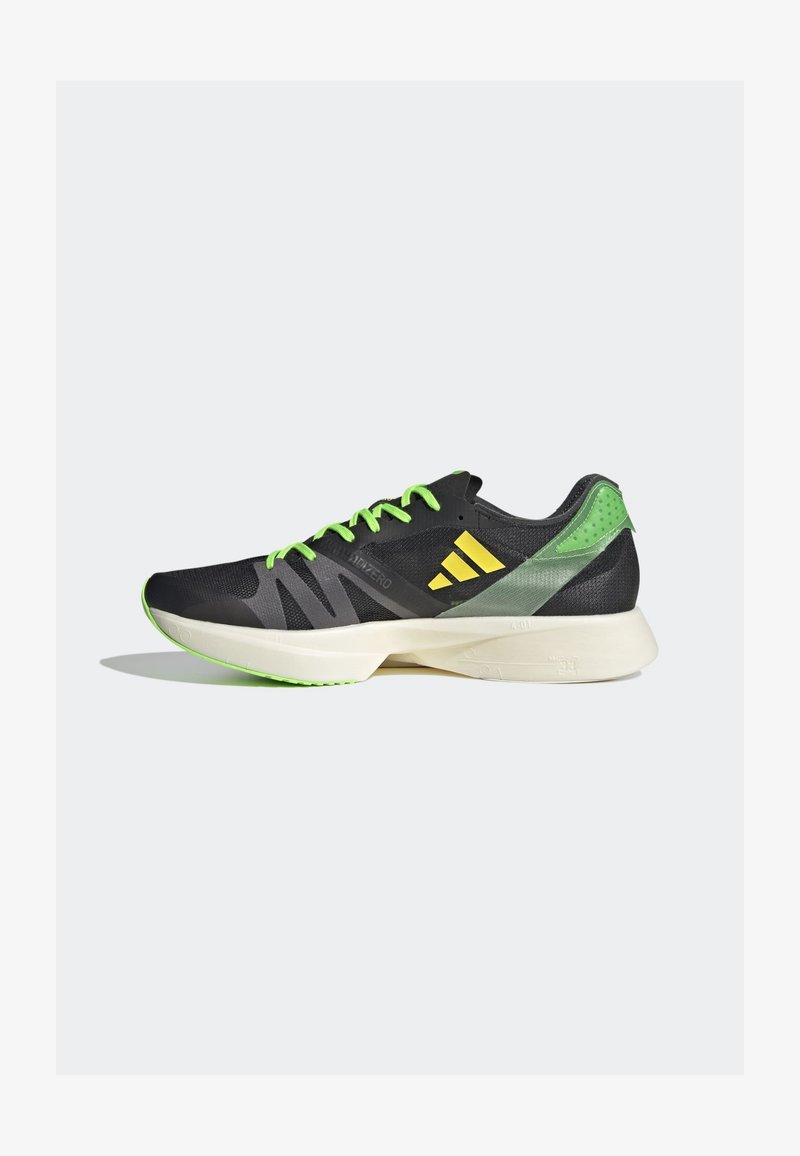 Chaussure de course noire et verte avec des accents jaune néon, des lacets verts et une semelle blanche rembourrée sur un fond clair uni.