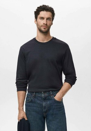 Black long-sleeve shirt made of cotton, fitted around the shoulders, paired with blue denim jeans, displayed on a neutral background.
