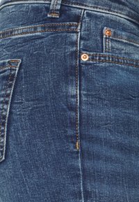 Modré džíny z denimu s úzkým střihem, s vybledlou strukturou, měděnými nýty a standardními kapsami, zdůrazňujícími klasické detaily šití.