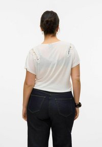 White short-sleeve shirt with embroidered lace accents on shoulders, paired with dark denim jeans featuring back pockets and a fitted waist.