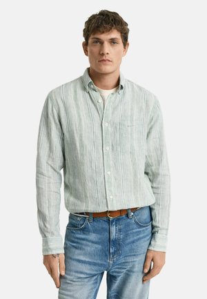 Camisa de rayas verde claro con cuello botón, bolsillo frontal y mangas largas. Llevada con jeans azules y un cinturón de cuero marrón.