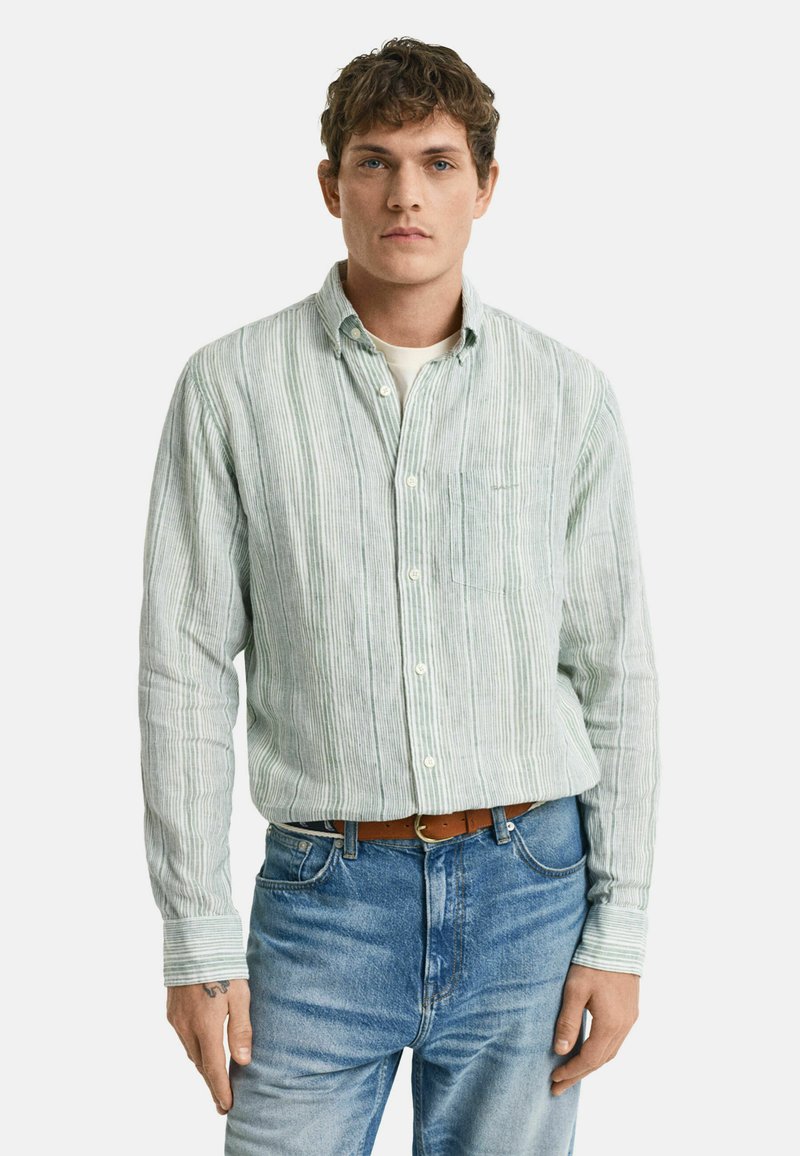 Camicia a righe verde chiaro con colletto alla francese, taschino frontale e maniche lunghe. Indossata con jeans blu e una cintura di pelle marrone.