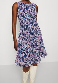 Robe à imprimé floral avec un corsage ajusté et une jupe évasée dans des nuances de bleu, violet et pêche. Le tissu semble léger avec une texture lisse.