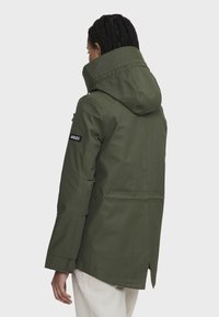 Parka olive avec capuche, dotée d'une fermeture éclair à l'avant, de poches latérales et d'un patch logo sur la manche gauche. Tissu lisse et mat.