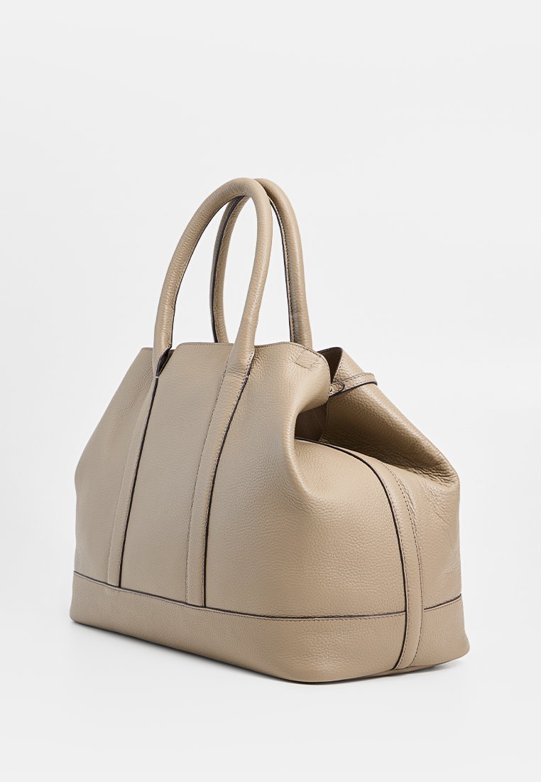 Beige leren boodschaptas met twee handvatten, voorzien van een zachte, gestructureerde afwerking en contrasterende donkere stiksels langs de zijkanten en onderkant.