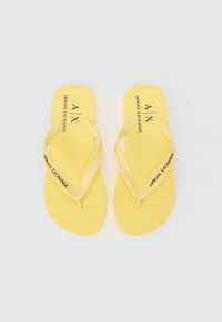 Gule flip-flopper med teksturert såle, med tynne stropper. På toppen står "ARMANI EXCHANGE" trykket i svart. Enkelt design, minimale detaljer.