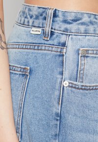 Pantalones cortos de mezclilla en un azul claro con cintura alta, con costuras naranjas, cierre de botón en la parte delantera y una pequeña etiqueta que dice "BILLABONG."